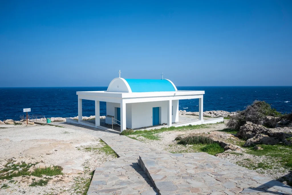 The white and blue Ayioi Anargyroi Chapel on the cliffs of Cape Greco National Park.